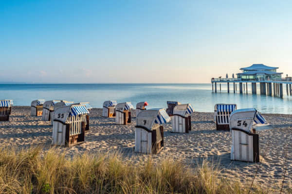 Strandkörbe auf dem Sand in Kühlungsborn, eine Brücke reicht ins Bild hinein von der rechten Seite ausgehend