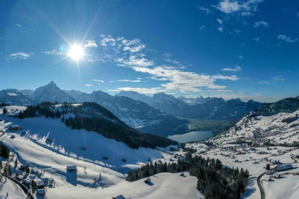 Ein Panorama Bild mit Sonnenschein, Bäumen und Schnee, kleine Skipiste