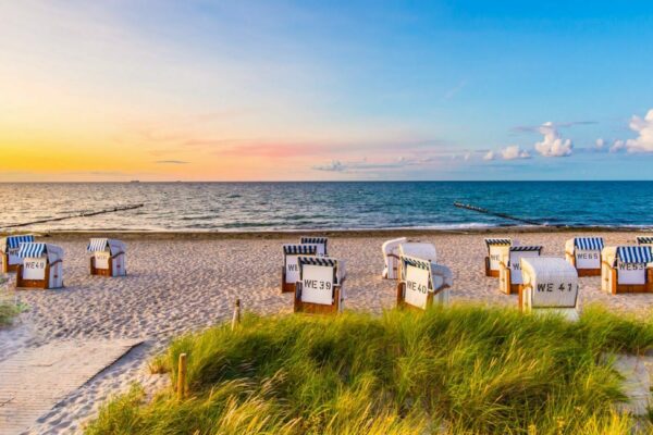 Ostsee Strand mit vielen Strandkörben, blauer Himmel, leichte Wolken und die Sonne scheint aufzugehen